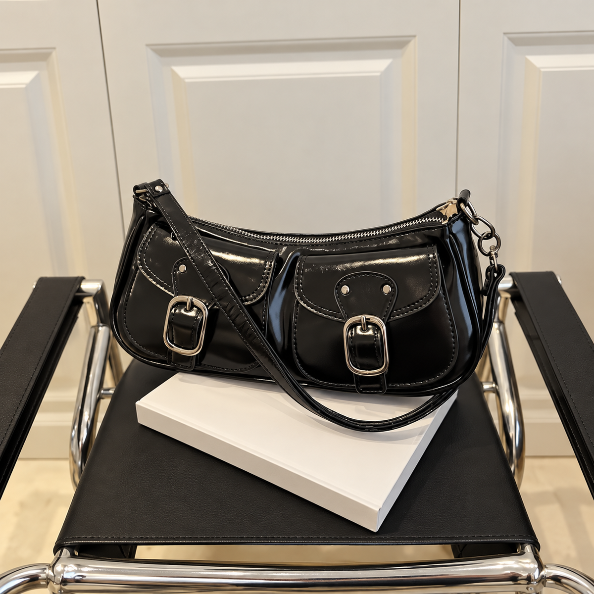 Black PU leather shoulder bag with front buckle details and a top zipper resting on a white book on a chair
