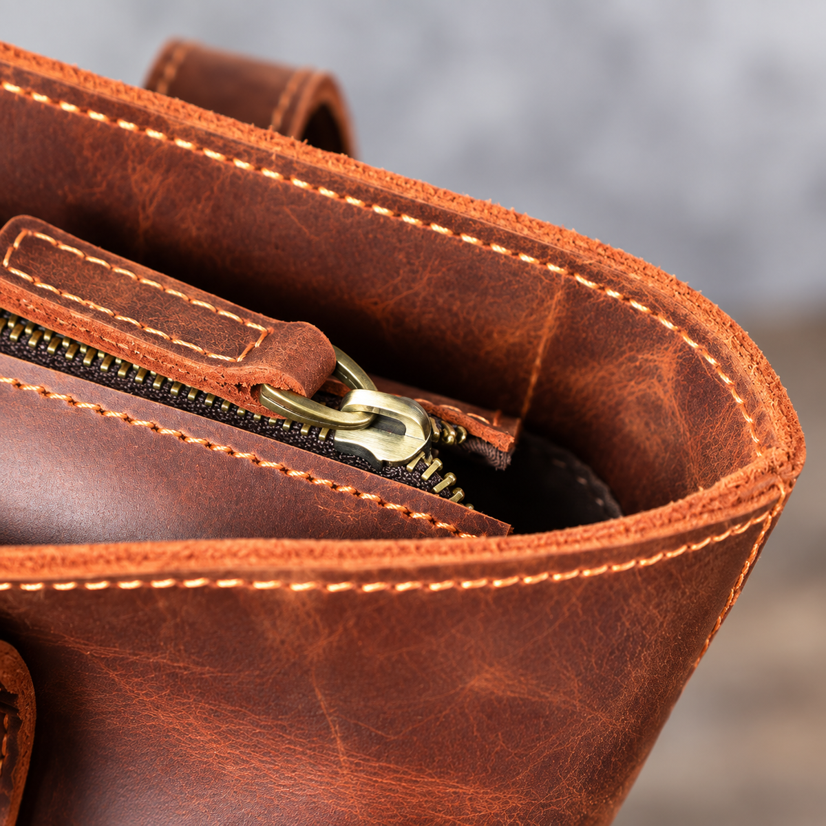 Close-up of the brown leather tote bag’s top zipper, leather pull tab and contrasting stitching.