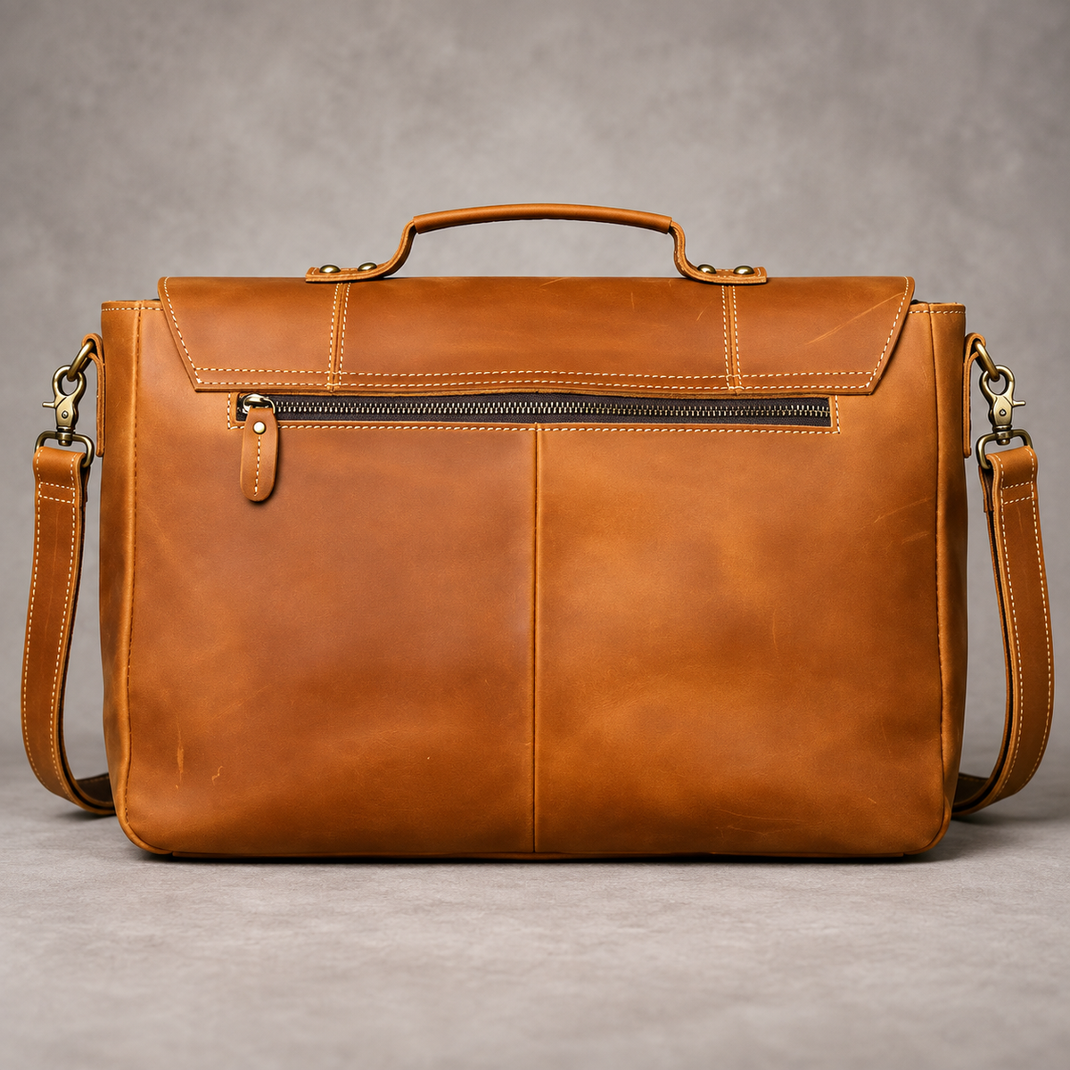 Rear view of a brown leather briefcase showing a horizontal zipper pocket, top handle and shoulder strap attachments